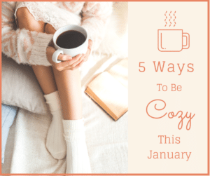 A cozy person in warm socks holds a mug of coffee while sitting with a book; text reads "5 Ways To Be Cozy This January" with a coffee cup icon.