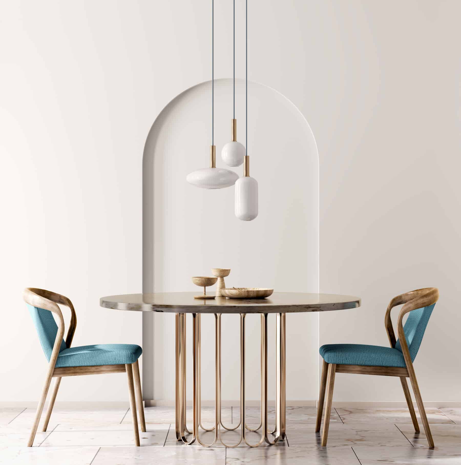 Modern dining area with two blue upholstered chairs and a round table, set against a white wall with an arched niche and three minimalist pendant lights above—a perfect example of Portland interior design for women.